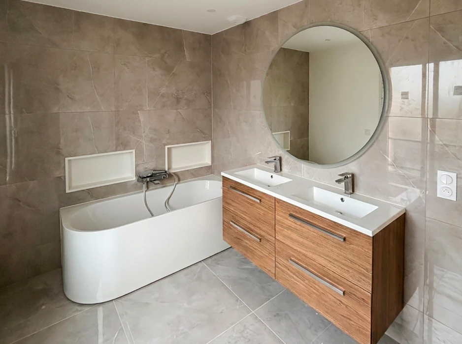 Salle de bain moderne avec baignoire asymétrique semi-îlot blanche, double vasque encastrée sur meuble suspendu en bois avec 3 tiroirs, miroir rond LED