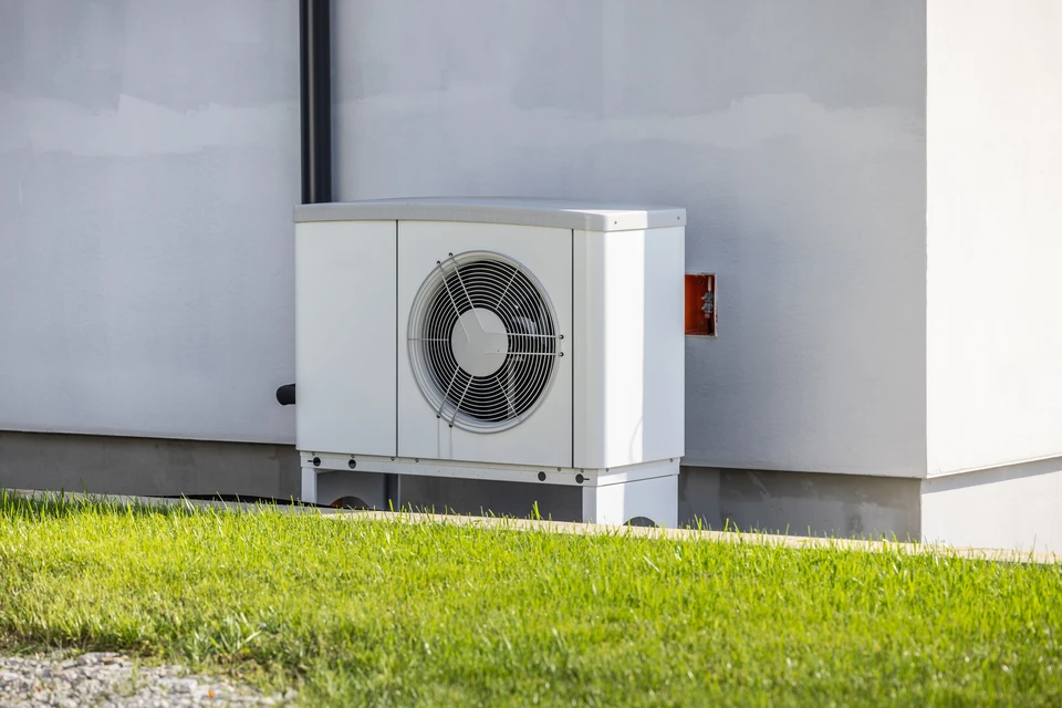 Plombier en uniforme bleu installant un radiateur à ailettes blanches dans une maison en construction