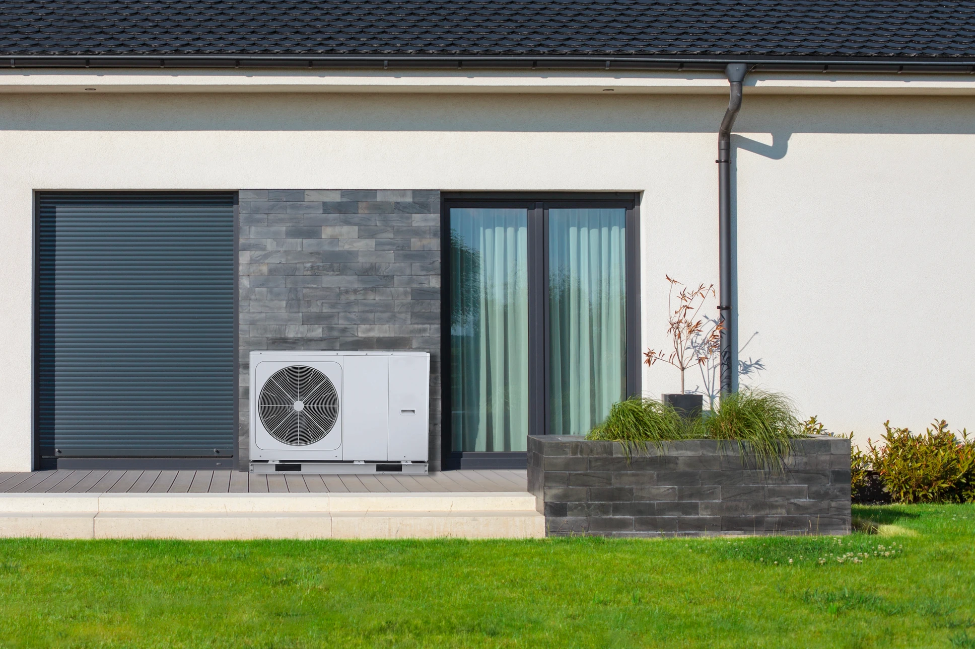 Technicien en climatisation travaillant sur une unité extérieure de pompe à chaleur devant un bâtiment moderne à bardage bois