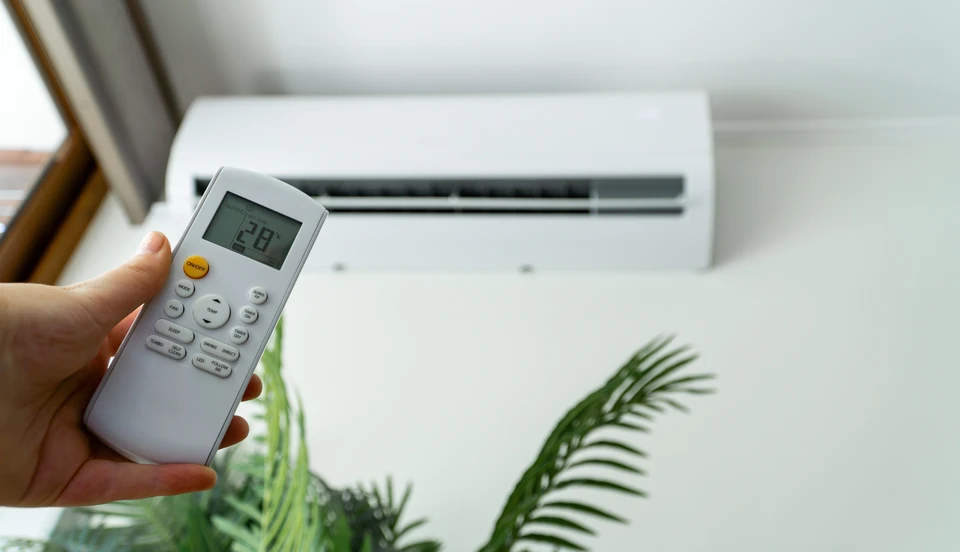 Technicien HVAC tenant un manifold de mesure de pression avec manomètres haute et basse pression, jaunes et rouges, devant une unité de climatisation extérieure résidentielle