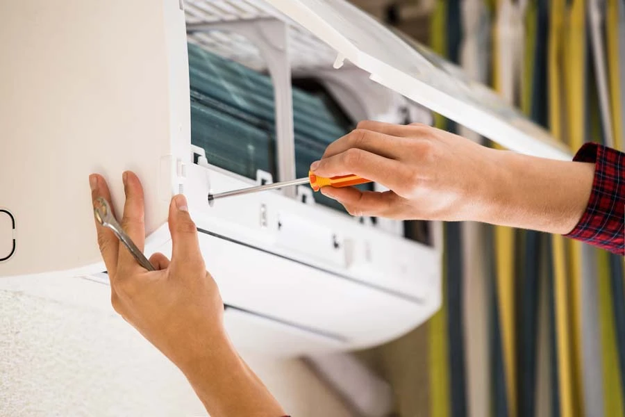 Un technicien en chemise grise installe ou répare une climatisation murale dans un intérieur moderne